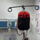 A full blood bag handing on a rack in a doctor's office.